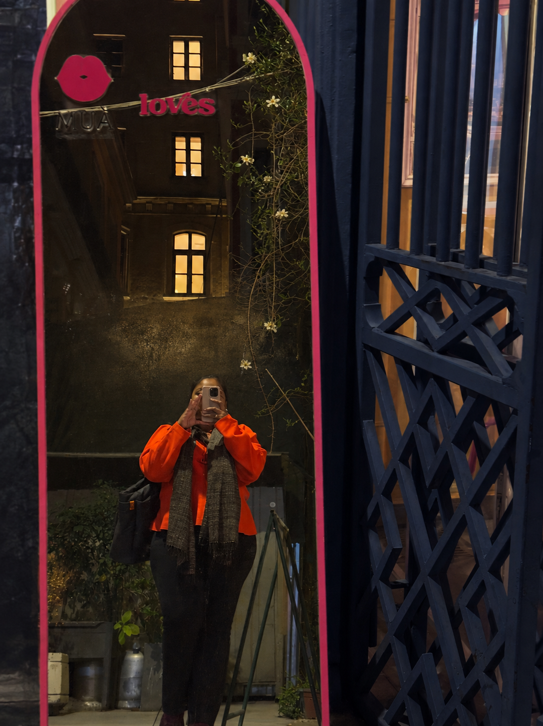 A woman in a tangerine coat taking a photograph in a tall mirror