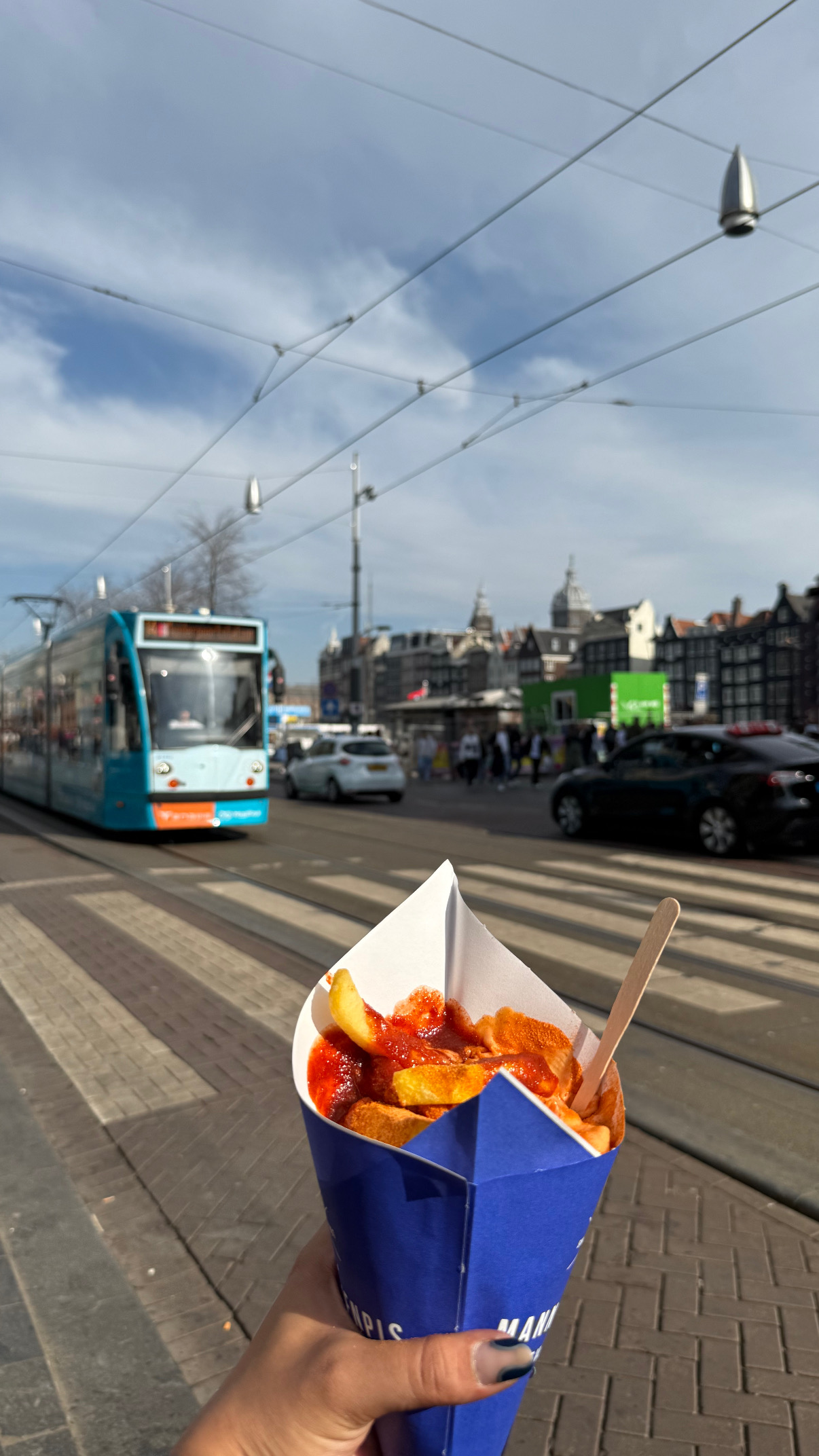 A paper cone of fries held on a city street